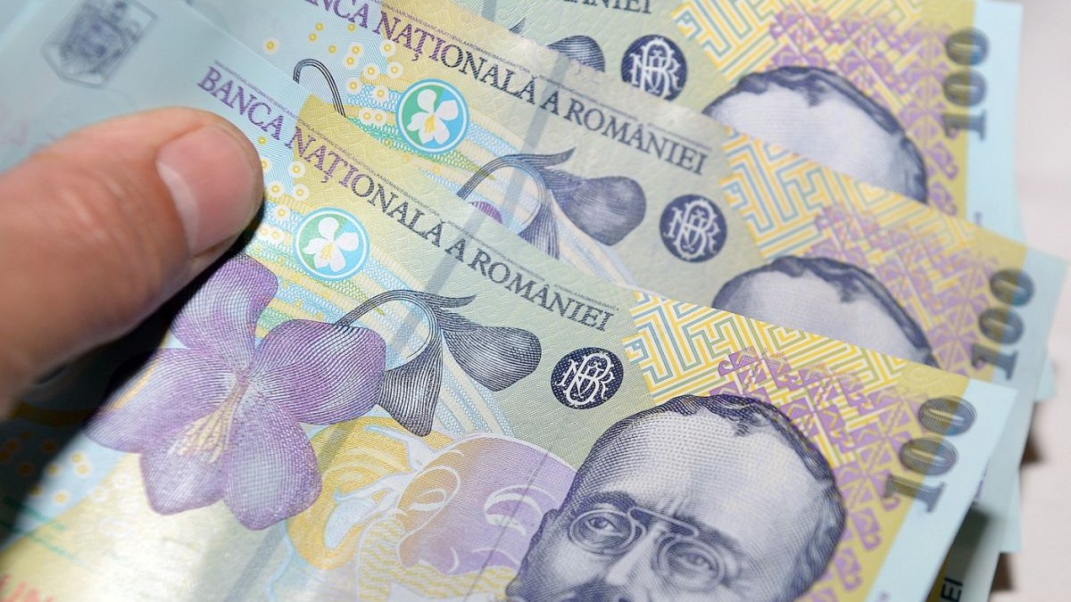 Un bărbat ține degetul pe trei bancnote de 100 de lei