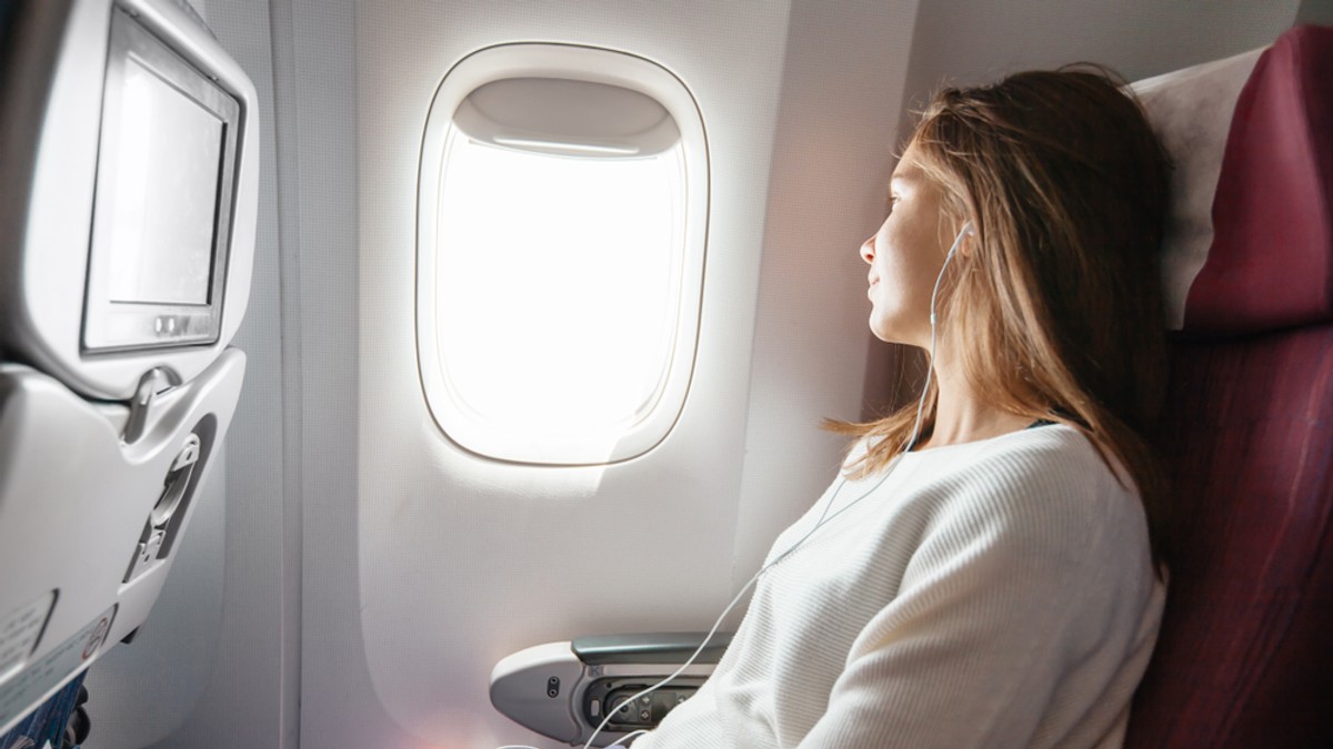 De ce este mereu frig în avion - Imagine cu o tânără aflată în avion, privind pe fereastră şi având o pătură pe picioare.