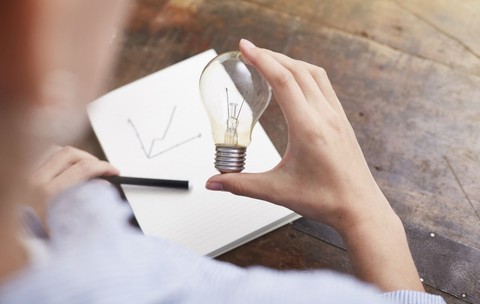 O femeie ține în mână un bec și planifică o metodă de economisire a energiei electrice. Foto: Profimedia Images