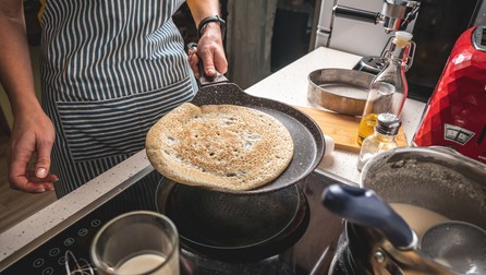 Woman is standing at the stove and frying pancakes in a hot pan. Concept of the process of making a delicious breakfast at home.
