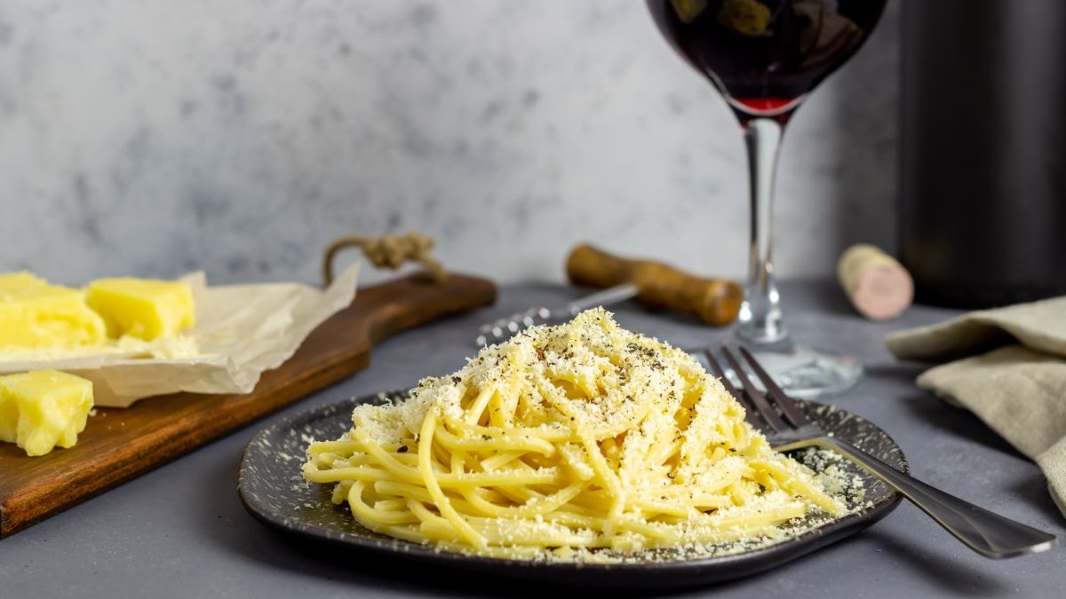 Spaghete în farfurie, pe masă alături brânză și un pahar cu vin roșu. Cacio e pepe