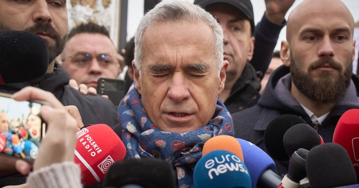 Călin Georgescu, candidatul de extremă dreapta, în timpul unu interviu, cu microfoane lângă el, cu un fular de culoare albastră la gât, și cu ochii închiși