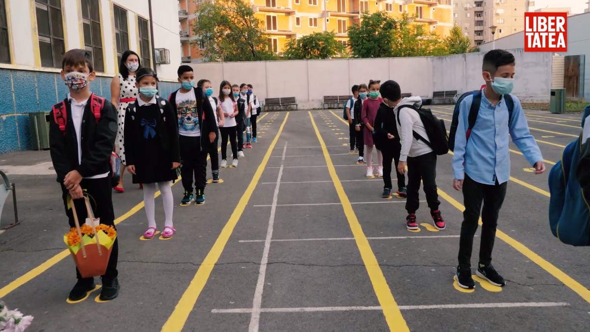 Mai muți elevi de la o școală din cartierul Ferentari din București stau aliniați în curtea școlii, cu măști pe față, pentru a intra în clase