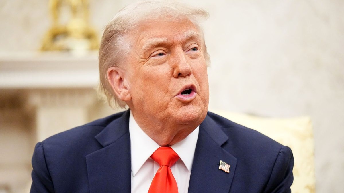 Donald Trump, îmbrăcat cu cămașă albă, cravată roșie și sacou bleumarin, surprins cu gura deschisă, în timp ce vorbește