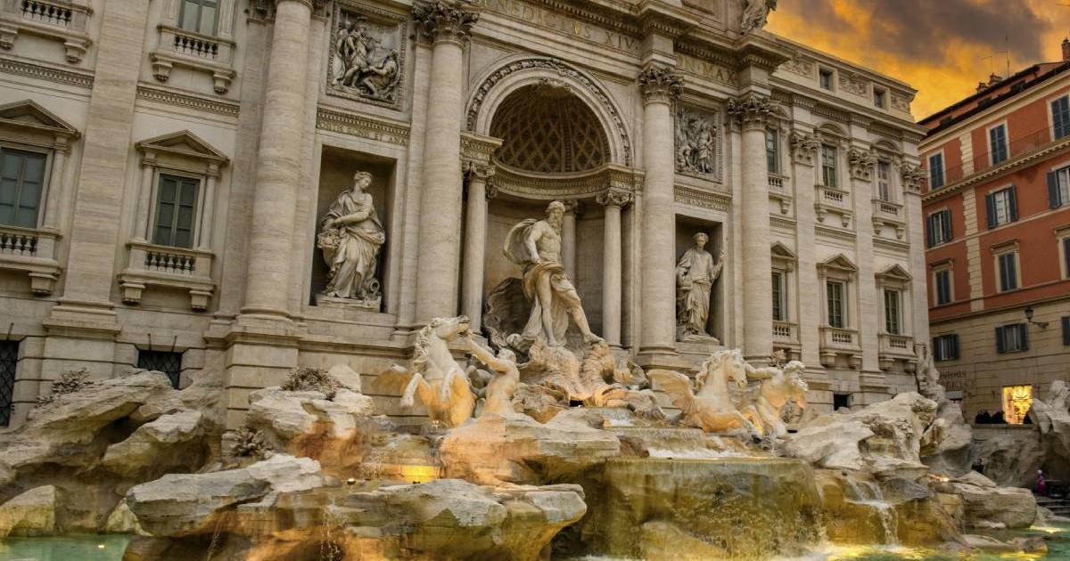 Vedere la apus în amurgul serii cu lumină calda, in nuante portocalii pe cer pe fântâna parțial iluminată Fontana di Trevi în centrul istoric al Romei, Roma, Lazio, Italia