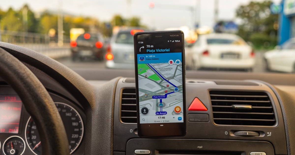 Interiorul unei mașini aflat în trafic, cu un telefon montat pe bord, afișând aplicația de navigație Waze.