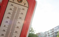 Un termometru de exterior în stil vintage, cu margine roșie, indicând o temperatură  de aproape 35°C în lumina soarelui.