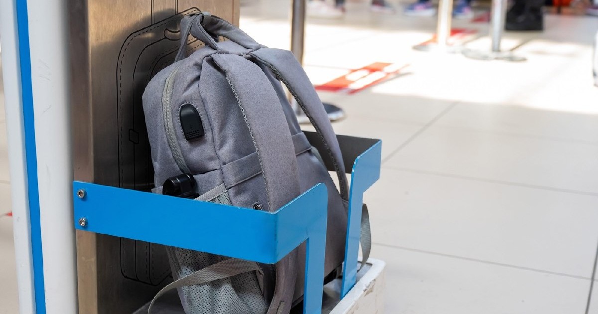 Un ghiozdan gri stă într-un suport metalic albastru pentru verificarea dimensiunii bagajelor de mână la aeroport.