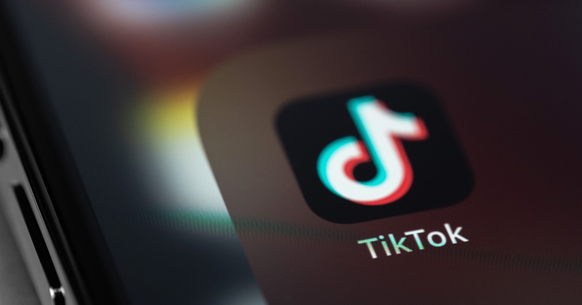 Imaginea arată logo-ul TikTok afișat pe ecranul unui smartphone, într-un prim-plan cu efecte de lumină și blur care sugerează tehnologie și dinamism. Vizualul transmite ideea de influență digitală și impact major al platformei în economia și publicitatea online.