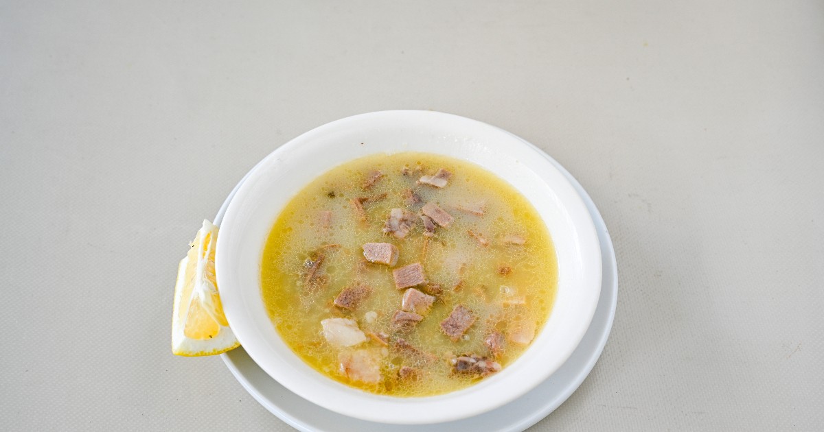 O porție de ciorbă de burtă este servită într-un bol alb, alături de o felie de lămâie. Preparatul are un aspect cremos, cu bucăți de carne vizibile, sugerând o rețetă tradițională consistentă.