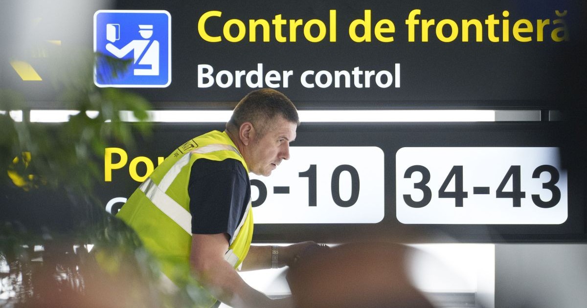 Un bărbat care poartă o vestă reflectorizantă de culoare verde, iar pe fundal un panou pe care scrie Control de frontieră și Border Control, la Aeroportul Otopeni