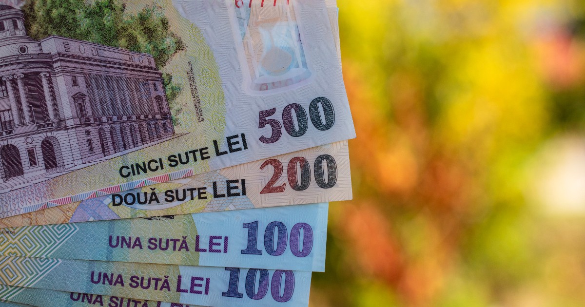 Imaginea prezintă mai multe bancnote românești de diferite valori (500, 200, 100 și 50 de lei), aranjate în evantai, cu un fundal colorat, neclar