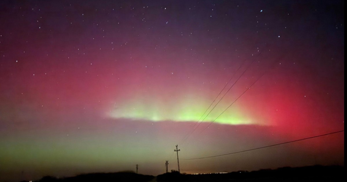 Aurora boreală în nuanțe de roșu și verde, vizibilă deasupra unui peisaj rural nocturn din județul Bihor.