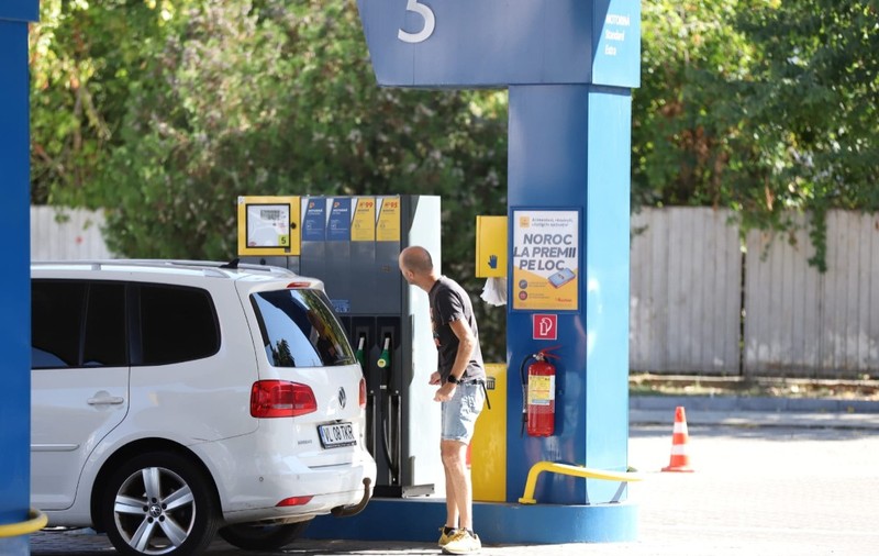 Un bărbat care se uită la ecranul unei pompe dintr-o stație de carburanți, lângă un autoturism alb Volkswagen parcat pentru alimentare. Foto: Libertatea/ Dumitru Angelescu