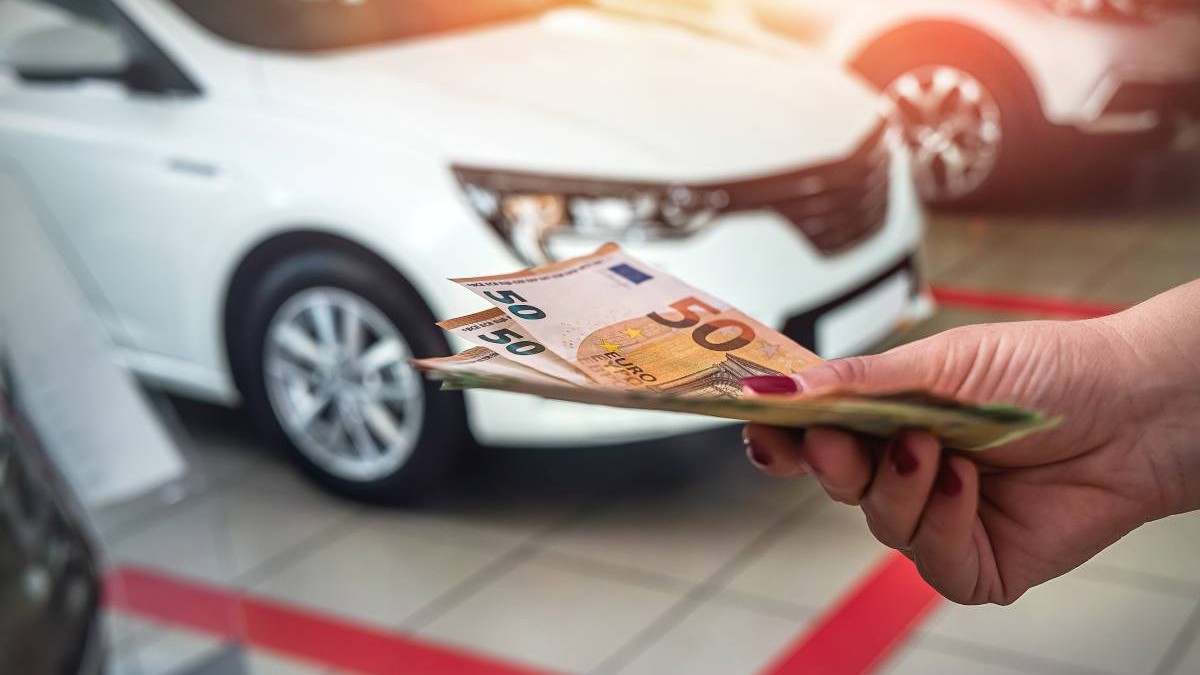 mana unei femei intine mai multe bancnote euro, in fundal se vad mai multe masini. Conceptul de vanzare masini second-hand