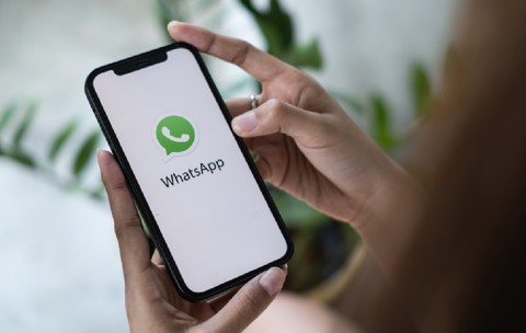 O femeie ține în mână un iPhone pe ecranul căruia este deschisă aplicația de mesagerie WhatsApp. 