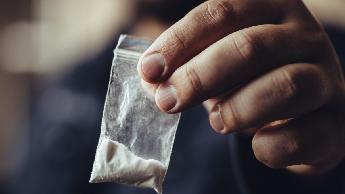 În imagine este ilustrat un bărbat care ține un plic cu droguri în mână