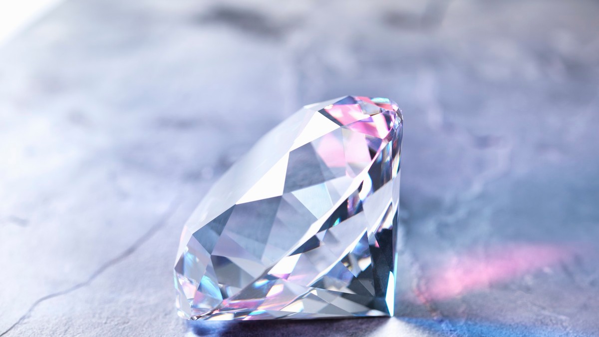 Imagine cu un diamant din care se reflectă lumină în diferite culori, așezat pe o masă lucioasă închisă la culoare