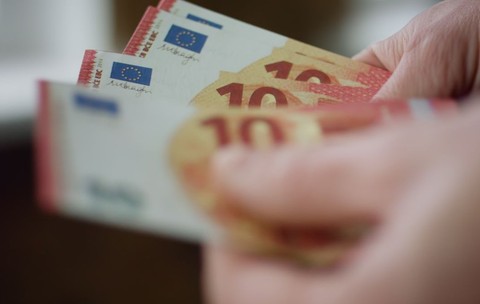 o mână care ține câteva bancnote de 10 euro, roșii și galbene