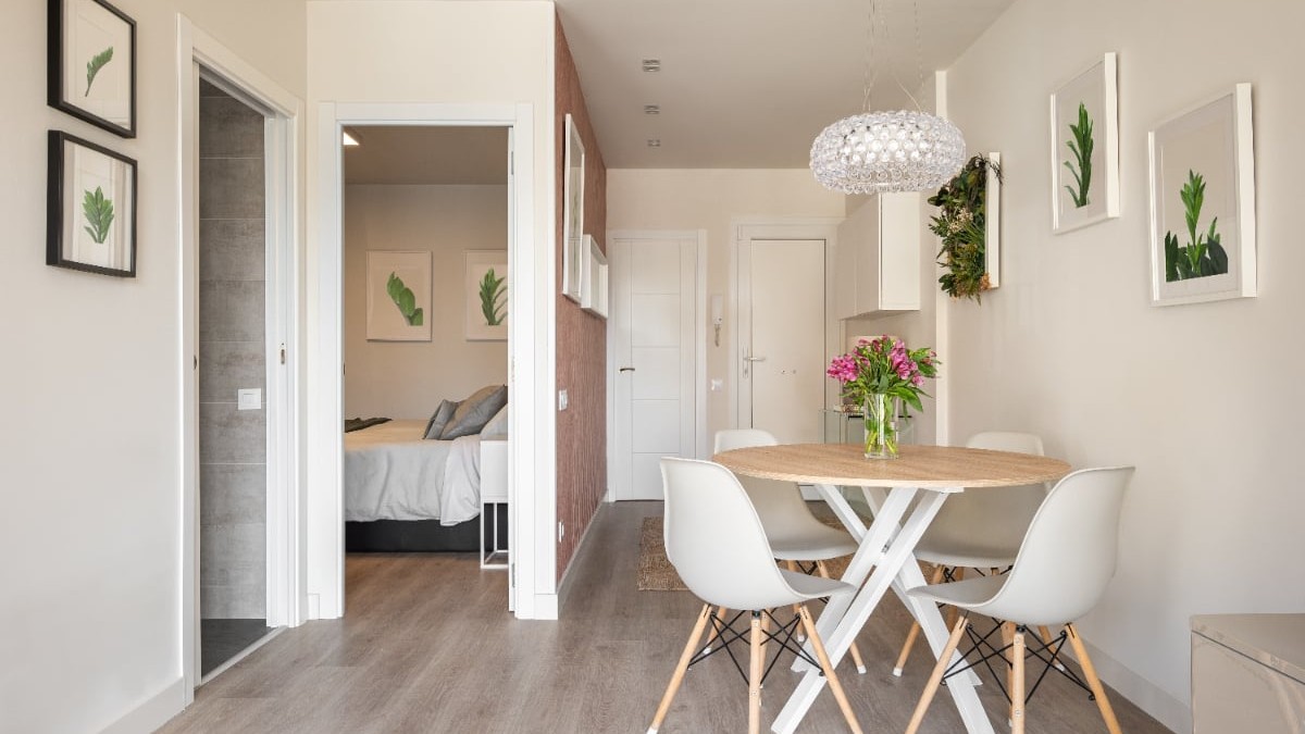 Un apartament mic cu mobila alba, masa si scaunele sunt albe, intrarea in dormitor se face direct din living