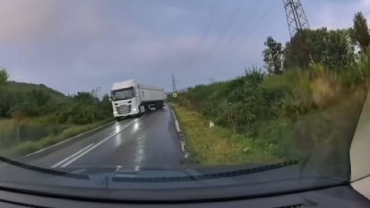Un TIR care derapează pe o șosea udă, este vorba despre un drum din România, înconjurat de arbori și vegetație