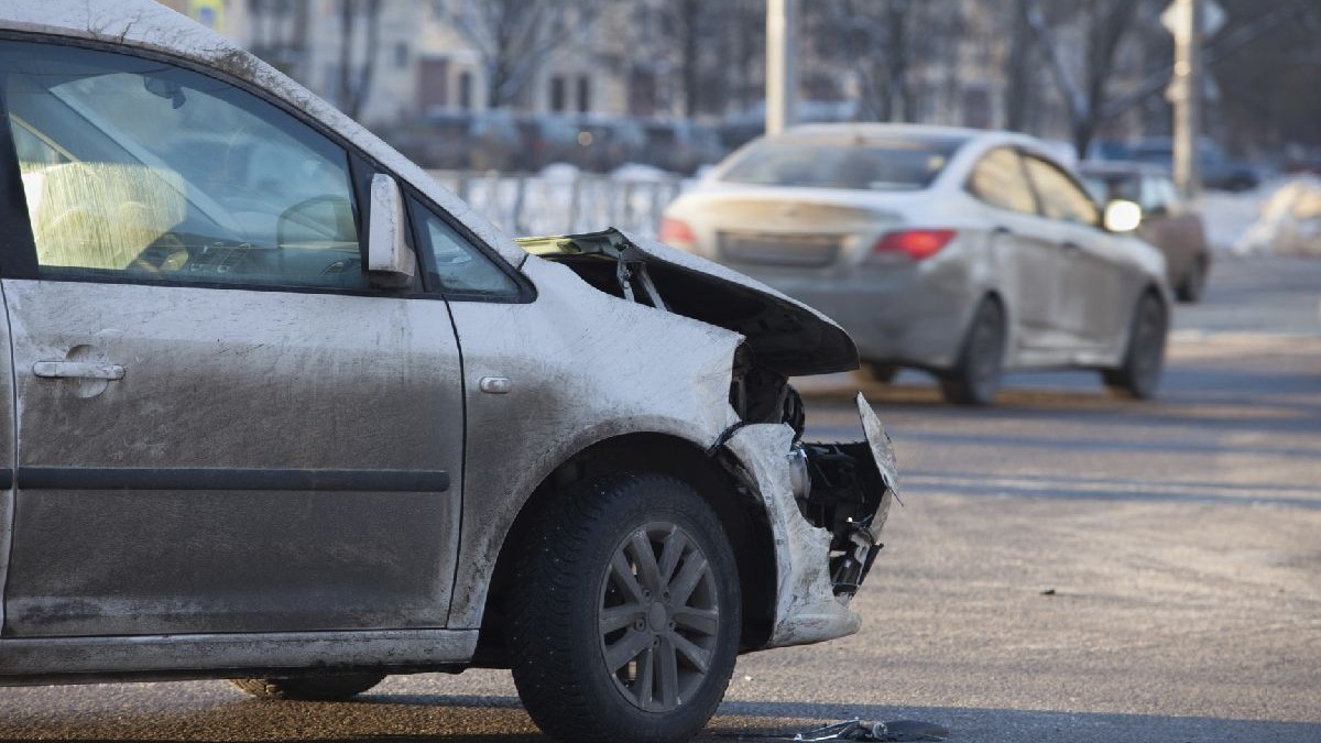 Fotografie cu un sedan alb cu partea frontală grav avariată, parcat pe o stradă înzăpezită, cu un sedan alb în fundal.