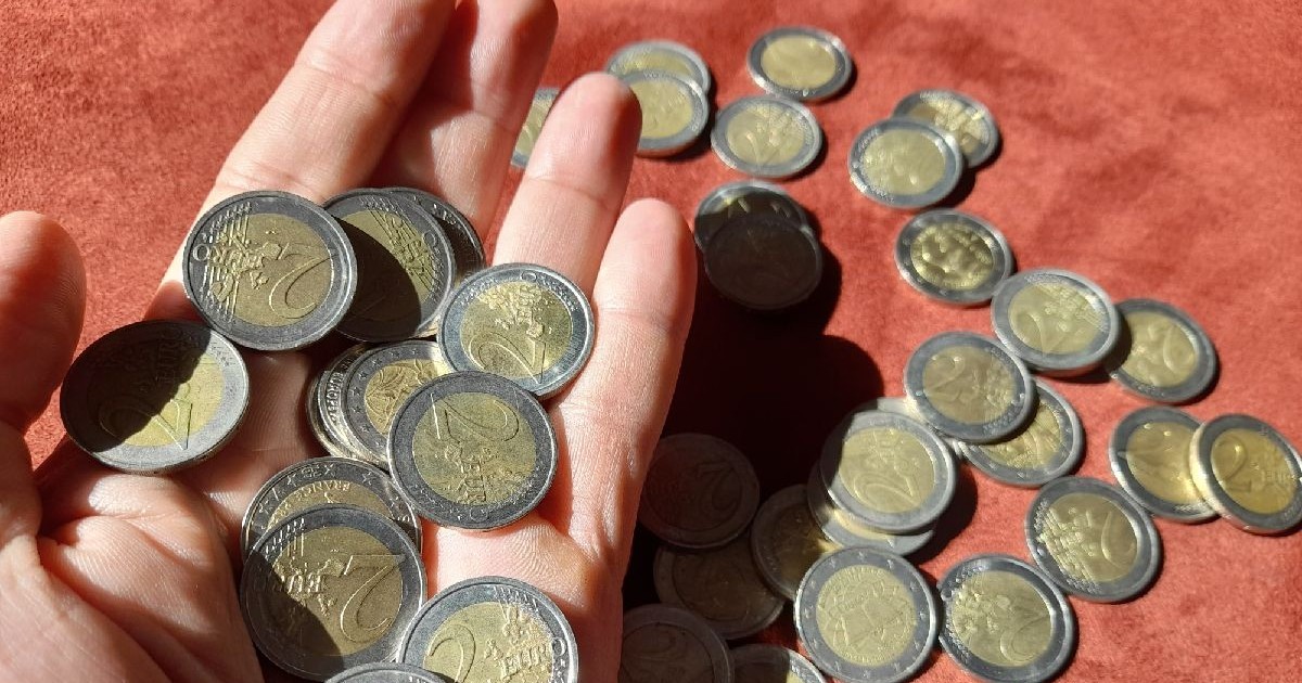 Prim-plan cu mai multe monede de 2 euro așezate în palma unui bărbat și pe o masă