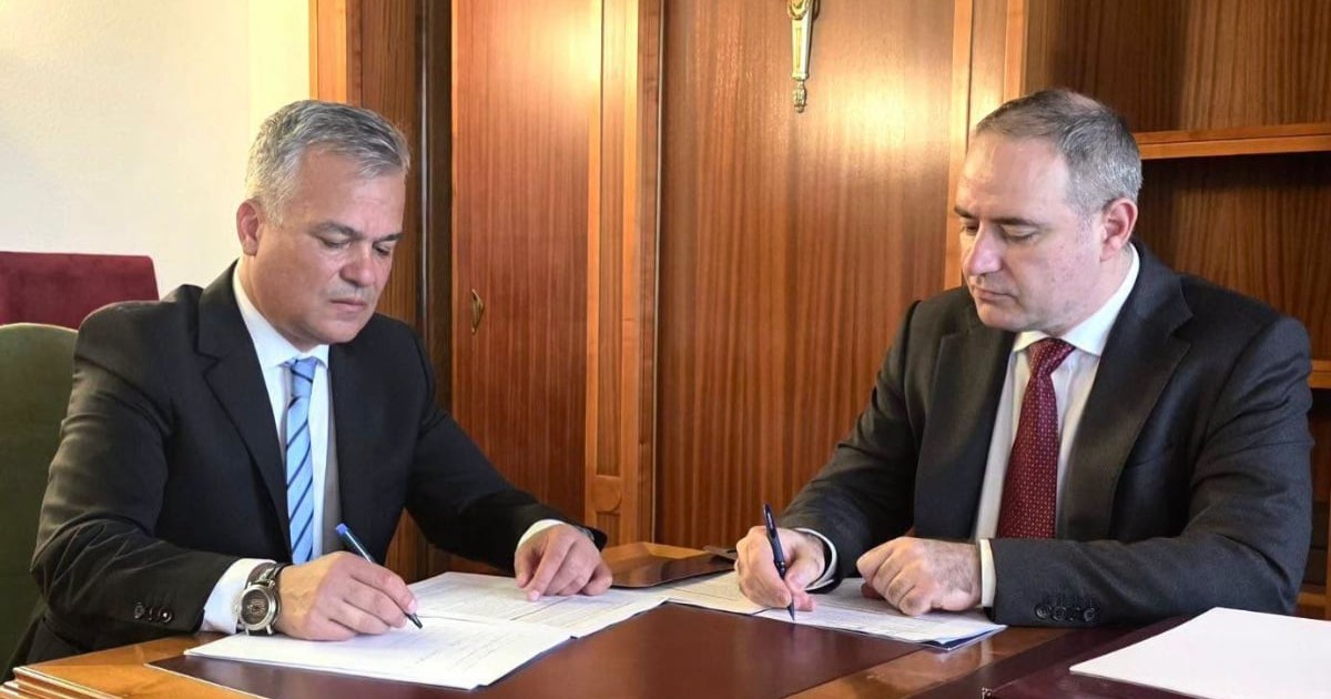 Adrian Veștea și Alexandru Nazare îmbrăcați în costume negre, așezați la un birou din lemn în timp ce semnează niște documente oficiale.