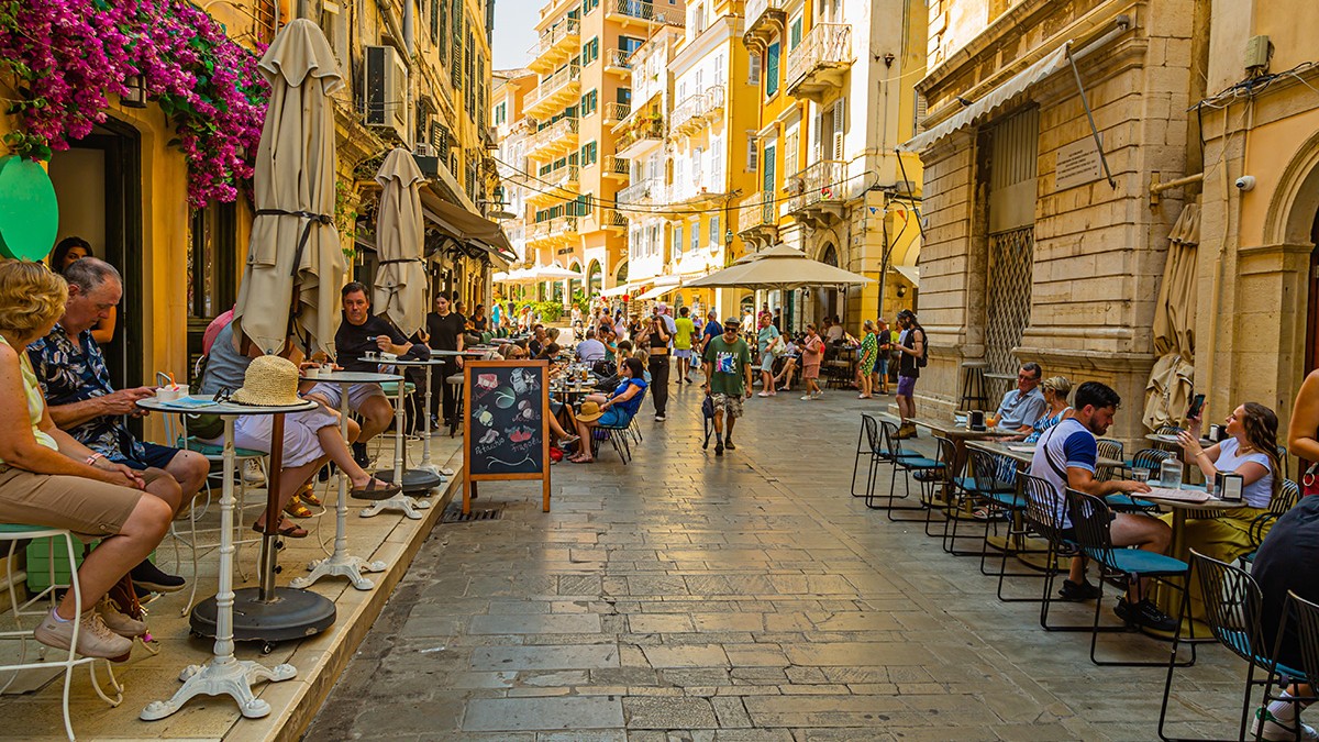 O stradă din Corfu cu rerstaurante și mulți clienți la mese.