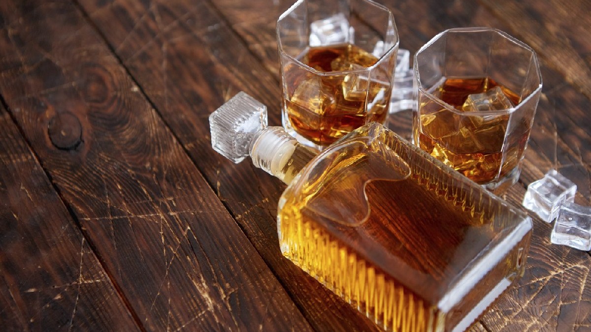 Sticlă de whisky cu două pahare așezate pe o masă rustică din lemn