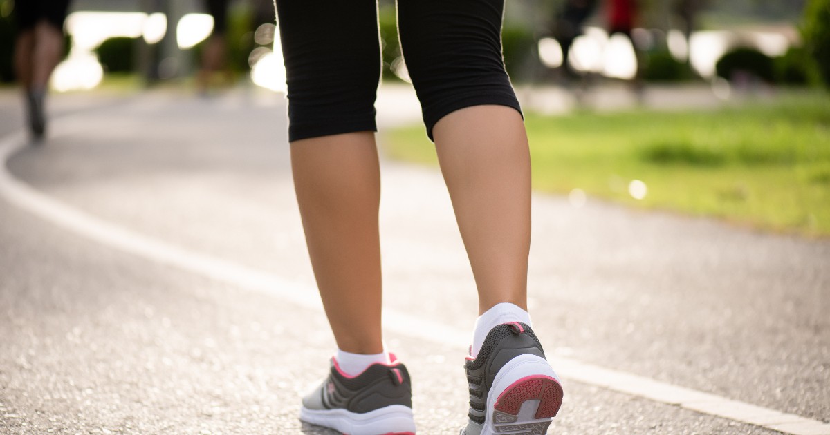 O persoană încălțată în adidași sport merge pe o alee din parc, într-o zi însorită. Imaginea transmite ideea de mișcare, stil de viață sănătos și activitate fizică zilnică.