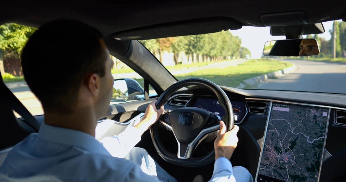Un bărbat brunet cu părul scurt, în timp ce stă la volan și conduce o mașină electrică pe o stradă din Europa