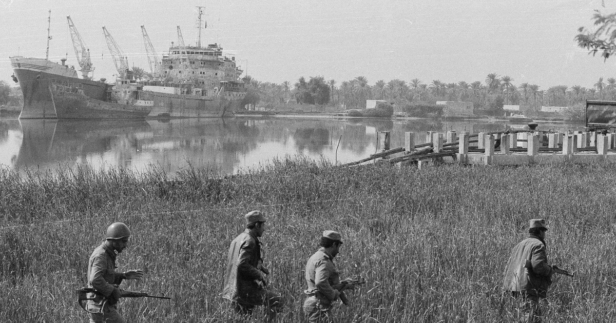 Soldați irakieni patrulează malul nordic al râului Karun, care separă acest oraș ocupat de Irak de insula iraniană asediată Abadan, 6 noiembrie 1980. În fundal sunt două dintre numeroasele nave avariate abandonate în port ca urmare a războiului.