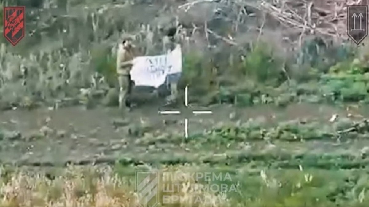 Doi soldați rusi ridică un steag alb pe un camp, în Ucraina, iunie 2025