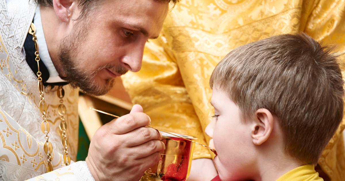 Sfânta Împărtășanie – reguli pentru credincioși - Imagine cu un preot care împărtăşeşte un copil
