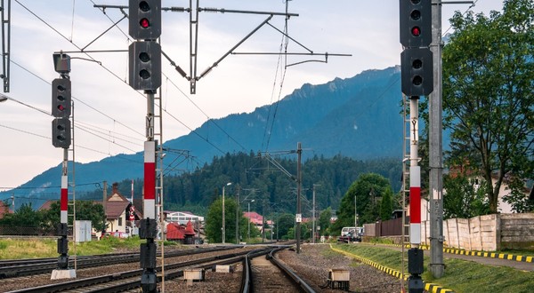 Trei linii de cale ferată într-o gară dintr-o zonă montană din România, luminile roșii de semnalizare sunt aprinse