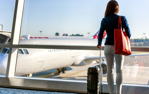 O turistă cu bagaje care priveşte apusul de soare pe fereastra unui aeroport. Imagine cu caracter reprezentativ.