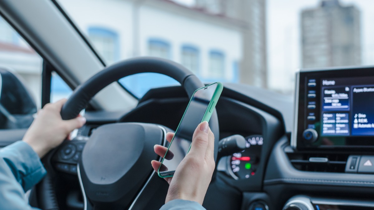 O femeie care ține telefonul în mână în timp ce e la volan.