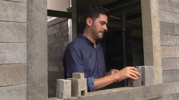 Imaginea prezintă un bărbat îmbrăcat în cămașă albastră care asamblează blocuri modulare din plastic reciclat pe glafurile unei ferestre în cadrul construcției unei case.