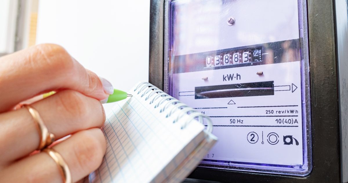 O femeie scrie cu un pic verde pe un carnețel indexul curentului electric, după ce a citit contorului de electricitate