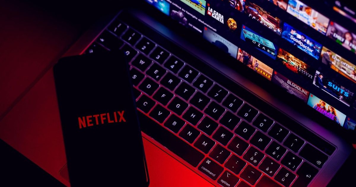 logo-ul aplicației de streaming netflix vazut pe ecranul unui smartphone, așezat pe un laptop deschis. pe ecranul laptopului poate fi vazuta interfata aplicației netflix