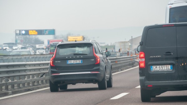 Trafic aglomerat de pe o autostradă din Italia pe vreme cețoasă, în prim-plan fiind vizibile partea din spate a unui SUV Volvo XC90 închis la culoare și a unei autoutilitare Fiat Scudo de culoare neagră.