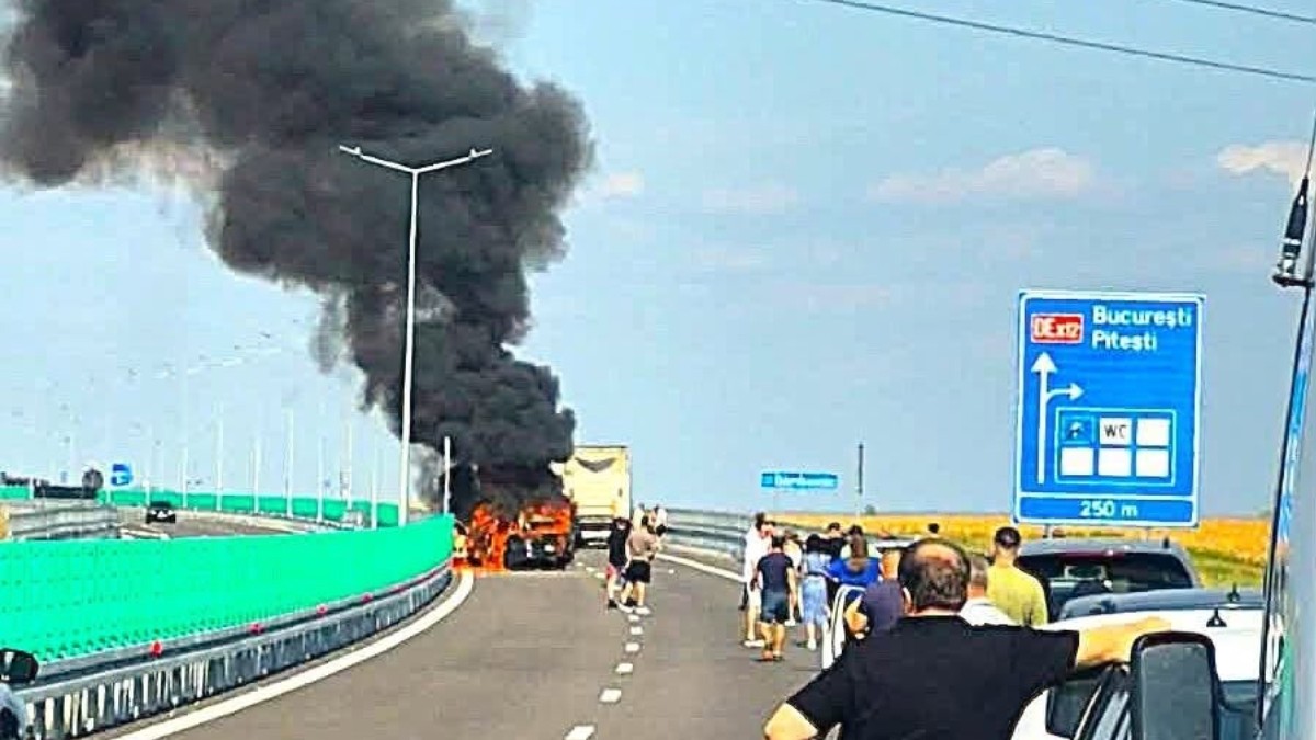O mașină care a luat foc pe o autostradă din România, autoturismul este in flăcări și deasupra lui se ede un nor negru de fum