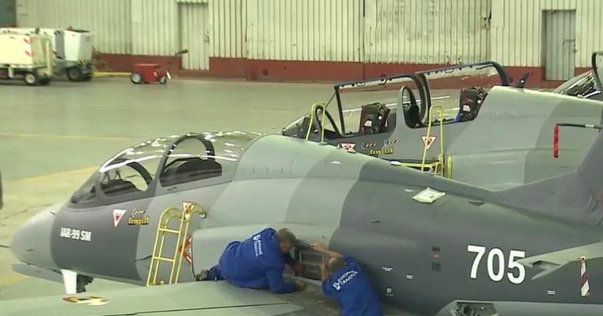 Doi ingineri de la Avioane Craiova, îmbrăcați în combinezoane albastre, lucrează la un avion IAR-99 SM de culoare gri, într-un hangar