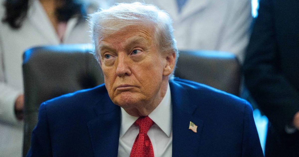 Donald Trump, îmbrăcat într-un costum, stă la un birou și privește dezamăgit