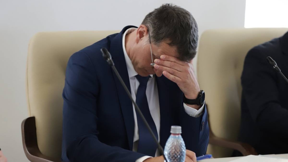 Ionuț Moșteanu, ministrul Apararii si membru USR, in sacou inchis la culoare, camasa amba si cravata neagra, asezat la birou, priving in jos, cu mana stanga peste ochi si frunte
