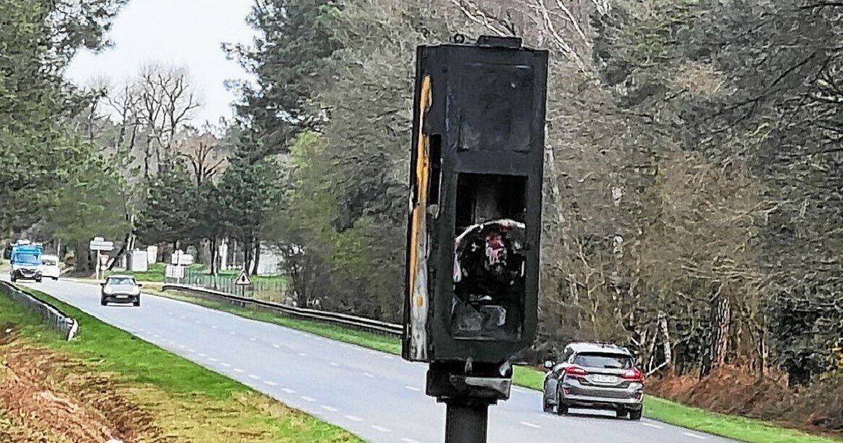 Imaginea surprinde o scenă de pe marginea unei șosele, având în prim-plan un radar auto incendiat. Carcasa metalică este înnegrită de funingine, deformată și prezintă urme de ardere.