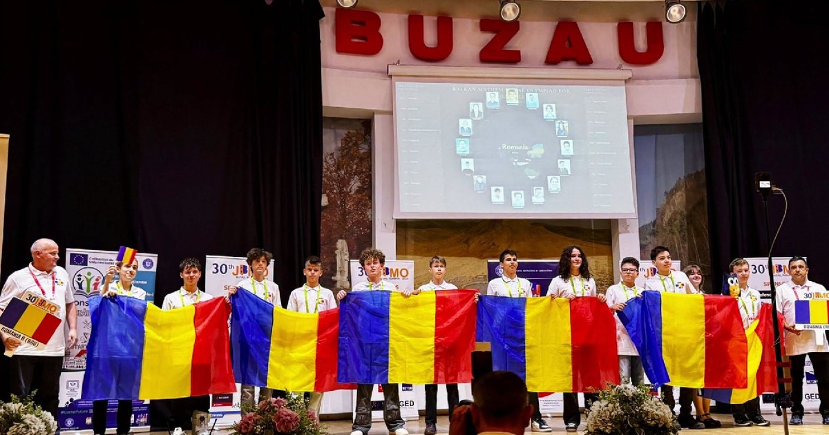 Mai multu elevi cu tricouri albe, pe o scena, deasupra căreia scrie Buzau, tin in mana steaguri ale României, la Olimpiada Balcanică de Matematică Juniori 2026