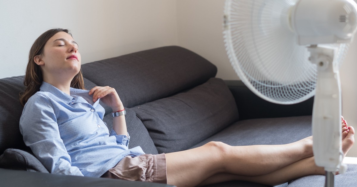Cele mai bune ventilatoare sub 500 de lei- O femeie sta pe canapea in fata unui ventilator
