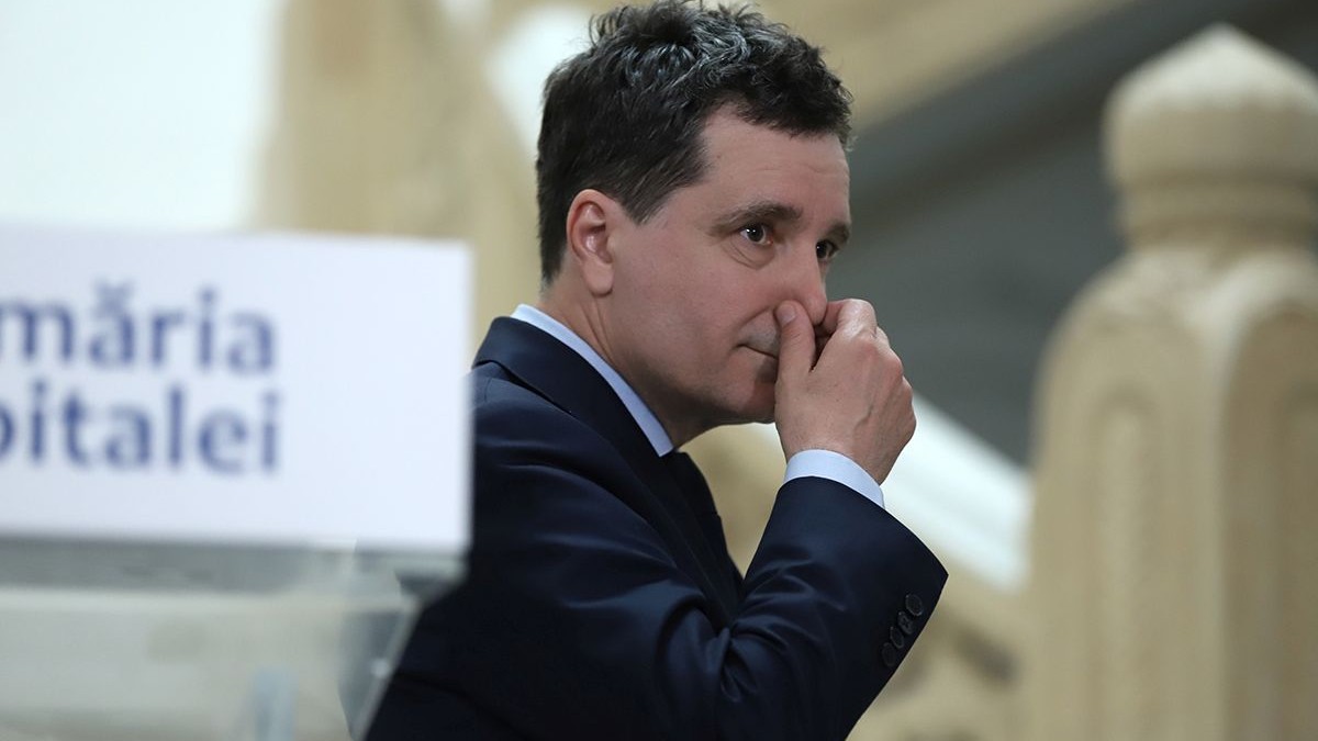 Nicușor Dan, îmbrăcat la costum, privește spre dreapta și se ține de nas, având în spate pupitrul de la Primăria București, 22 aprilie 2025